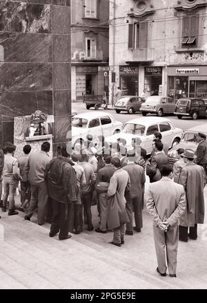 1950S MENSCHENMENGE ANONYMER LEUTE MÄNNER FRAUEN UND KINDER SCHAUEN SICH DIE PUPPENTHEATER NAPLES ITALIEN AN - R5666 MAY001 HARS SHOPS AUTOMOBIL MÄNNER PERFORMANCE ENTERTAINMENT TRANSPORT EUROPE B&W HIGH ANGLE ADVENTURE EUROPEAN AND AUTOS AUFREGEND RECITATION ITALY OPPORTUNITY STORES CONNECTION AUTOS STÄDTE STELLEN SICH FAHRZEUGE AUS DEM SÜDOSTEN VOR, ANONYME NEAPOLITANISCHE KREATIVITÄT NEAPEL SCHWARZWEISS WEISSE ETHNISCHE ZUGEHÖRIGKEIT ALTMODISCHE SCHAUFENSTERFRONTEN Stockfoto