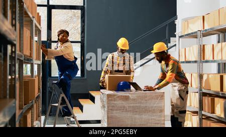 Team von Kollegen, die Produkte auf Regalen und Regalen organisieren und an der Verwaltung von Verbrauchsmaterialien arbeiten. Lagermitarbeiter, die den Transport für den Versand von Einzelhandelsbestellungen planen. Handgeführte Aufnahme. Stockfoto