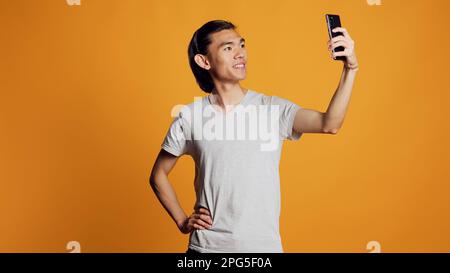 Glücklicher Kerl, der Fotos macht und sich sorgenfrei benimmt, lächelt und für Fotos auf dem Handy posiert. Junges fröhliches Model, das Bilder auf dem Smartphone macht, auf der Social-Media-Seite postet, Hipster-Look. Stockfoto