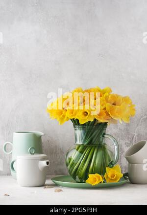 Wunderschönes Frühlingsblumen-Arrangement mit gelben Narzissen in einer alten Glaskanne. Hausgemachte Dekoration für Ostern oder Muttertag. Speicherplatz kopieren. Stockfoto