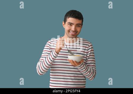 Junger Mann isst Cornflakes mit Löffel auf farbigem Hintergrund Stockfoto