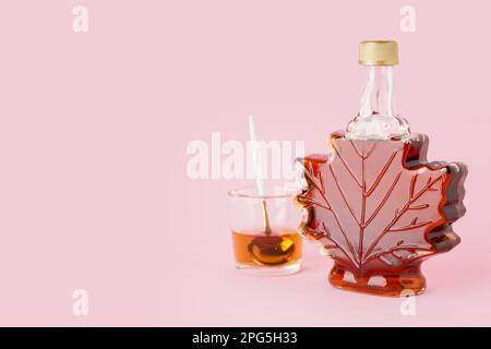 Flasche und Löffel in einem Glas leckeren Ahornsirups auf rosa Hintergrund Stockfoto