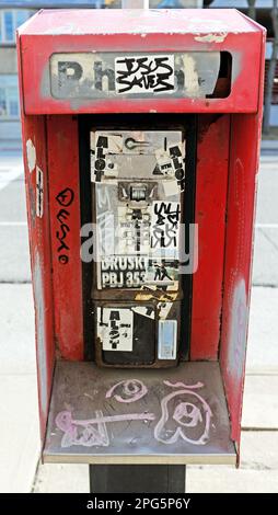 Ein altes rotes öffentliches Münztelefon, das durch Graffiti und Vandalismus schwer beschädigt wurde, hat noch keinen Empfänger an der Stange in Cleveland, Ohio, USA. Stockfoto