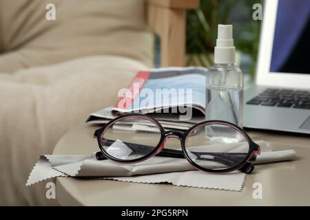 Brille, Mikrofasertuch und Sprühflasche auf dem Tisch im Innenbereich Stockfoto