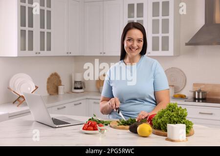 Schöne übergewichtige Frau, die eine gesunde Mahlzeit am Tisch in der Küche zubereitet Stockfoto