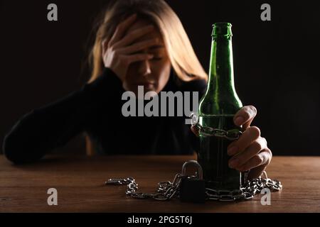 Alkoholsucht. Frau mit einer Flasche Bier an einem Holztisch vor schwarzem Hintergrund angekettet, konzentriert euch auf die Hand Stockfoto