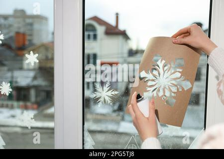 Eine Frau, die zu Hause Schneespray benutzt, um Fenster mit
