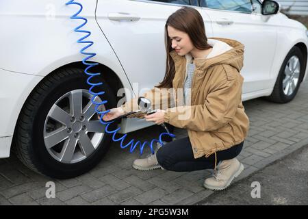 Junge Frau, die beim Autoservice Reifen aufpumpt Stockfoto