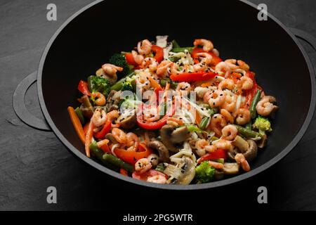 Gebratene Nudeln mit Pilzen, Garnelen und Gemüse in Wok auf schwarzem Tisch umrühren, Nahaufnahme Stockfoto