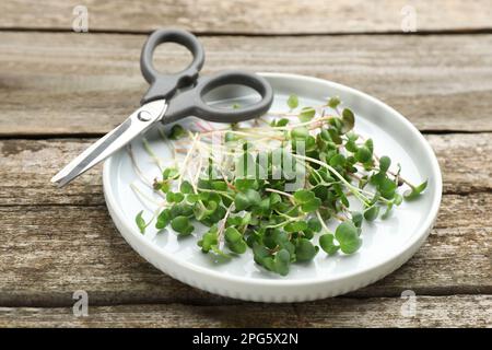 Platte mit geschnittenem frischen Rettich-Mikrogreens und Schere auf Holztisch Stockfoto