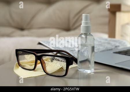 Brille, Mikrofasertuch und Sprühflasche auf dem Tisch im Innenbereich Stockfoto