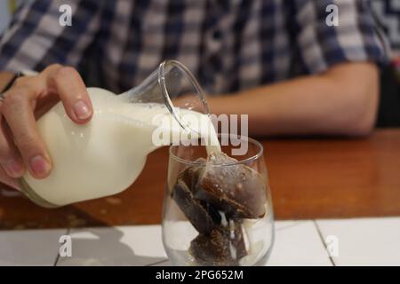 Milch, die in Glass Iced Coffee auf dem Tisch in einem Café gegossen wird. Stockfoto