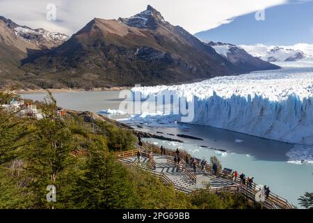 Touristen stehen auf einer hölzernen Plattform und bewundern den malerischen Perito-Moreno-Gletscher an einem sonnigen Tag im Los Glaciares-Nationalpark, Patagonien, Argentinien Stockfoto