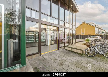 Einige Fahrräder parken vor einem Gebäude mit großen Fenstern auf beiden Seiten der Straße, es gibt einen leeren Parkplatz Stockfoto