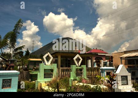 Ein ländlicher Friedhof im Hintergrund des Mount Lokon, einem aktiven Vulkan in Tomohon, Nord-Sulawesi, Indonesien. Stockfoto