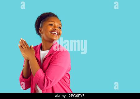 Fröhliche lächelnde junge afroamerikanische Frau mit Händen in Gebetsgesten auf blauem Hintergrund. Stockfoto