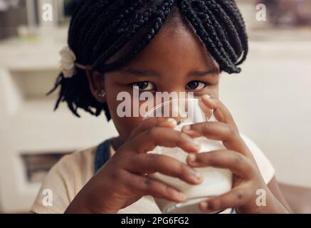 Ich bekomme nur meine tägliche Dosis Kalzium. Porträt eines bezaubernden kleinen Mädchens, das zu Hause ein Glas Milch trinkt. Stockfoto