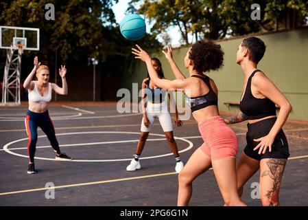 Endlich eine Pause, um den Ball zu übergeben. Eine vielfältige Gruppe von Sportlerinnen, die tagsüber gemeinsam ein Wettkampfspiel mit Basketball spielen. Stockfoto