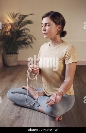 Nimm dir Zeit, um deine Seele glücklich zu machen. Aufnahme einer attraktiven jungen Frau, die drinnen sitzt und mala-Perlen während ihrer Meditationsroutine verwendet. Stockfoto