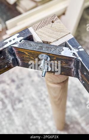 Holzschnittiger Schenkel aus massiver Eiche mit Metalltischrahmen während des Herstellungsprozesses des Esstisches in der Werkstattnahansicht Stockfoto