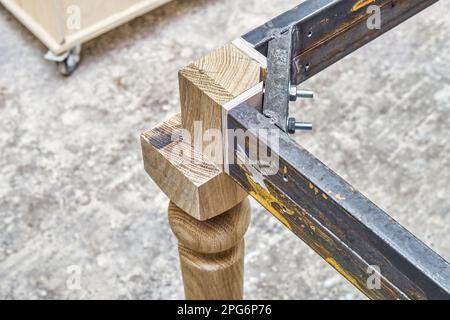 Holzschnittiger Schenkel aus massiver Eiche mit Metalltischrahmen während des Herstellungsprozesses des Esstisches in der Werkstattnahansicht Stockfoto