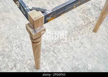 Holzschnittiger Schenkel aus massiver Eiche mit Metalltischrahmen während des Herstellungsprozesses des Esstisches in der Werkstattnahansicht Stockfoto