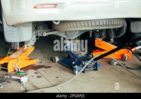 Ein Mechaniker hebt ein Auto mit drei Wagenhebern in einer Autoreparaturwerkstatt an, um das Problem zu prüfen, Wartungskonzept für das Fahrzeug Stockfoto