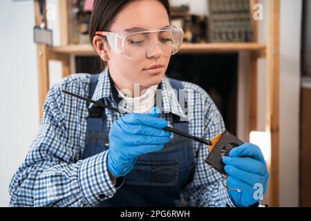 Laptop-Reparatur. Zerlegte Computerteile. Elektronische PC-Komponenten. Frau reinigt Laptop-Ventilator mit Bürste. Stockfoto