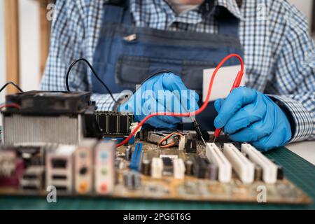 Nahaufnahmen von Technikerinnen, die die elektrische Spannung der Computerplatine mit Hilfe eines Multimeters messen. Wartung und Reparatur von Computerhardware Stockfoto