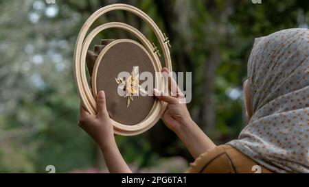 Eine Frau hält einen Korb mit Stickerei aus Holz mit Blumenmotiv in den Händen. Stockfoto