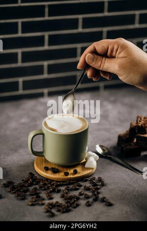 Eine Person löffelt frisch gebrühten Kaffee in eine Keramiktasse auf einem Tisch. Stockfoto