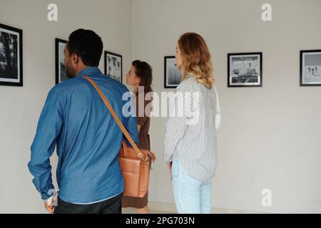 Eine Gruppe interkultureller Studenten oder Gäste in Freizeitkleidung, die vor einer Wand mit Kunstwerken stehen, während sie die Galerie der modernen Künste besuchen Stockfoto