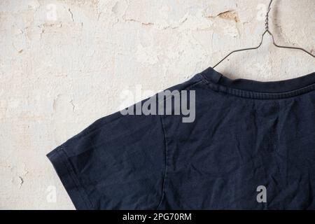 Dunkelblaues T-Shirt auf Kleiderbügeln an einer alten weißen Wand wie ein Moket Stockfoto