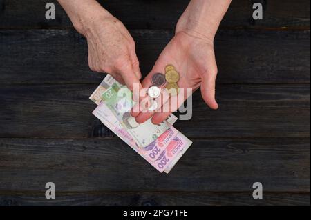 Eine ältere Frau hat Bargeld in der Hand und zählt es. Nahaufnahme der Hände einer alten Großmutter, die Hrywna-Banknoten auf den Tisch legt. Das Konzept von Stockfoto