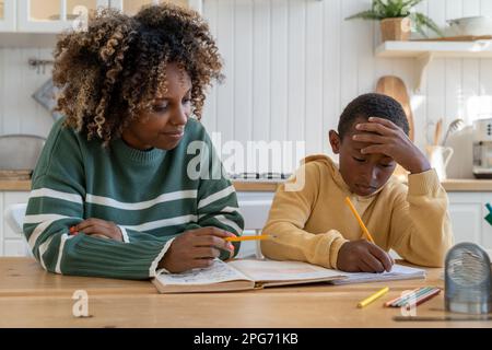 Fokussierte, birassistische Tutorin gibt Privatunterricht, rücksichtsvoller Kinderschüler am Schreibtisch zu Hause Stockfoto