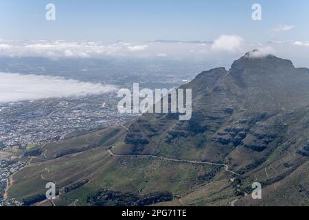 Landschaft mit gewundenen Straßen an östlichen Hängen des Tafelbergs mit niedrigen Wolken im Hintergrund, aufgenommen in hellem Sommerlicht in Kapstadt, Wes Stockfoto