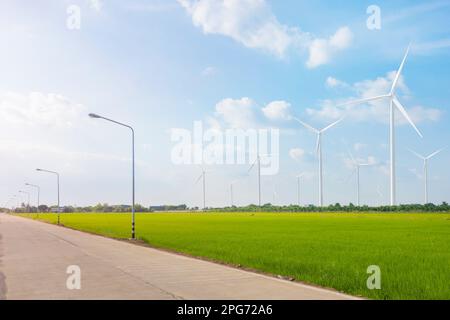 Betonstraße im ländlichen Thailand durch grüne Felder und Windkraftanlage im Hintergrund zur Erzeugung sauberer, umweltfreundlicher und nachhaltiger El Stockfoto