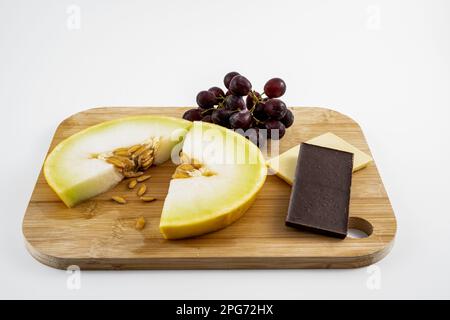 Nach dem Abendessen gibt es frische Honigtau-Melonenscheiben mit Trauben und weißer und dunkler Schokolade, isoliert auf weißem Hintergrund Stockfoto