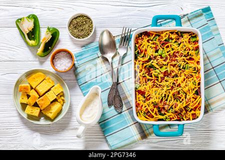 pinto Beans Speck Maisbrotsalat mit Tomaten, Paprika, Mais und Cheddar Käse in rechteckiger Schüssel auf weißem Holztisch mit Löffel und Gabel, Horizont Stockfoto