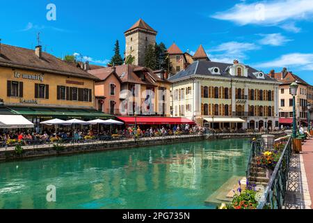 Blick auf den Kanal entlang der Promenade mit Restaurants im Freien und bunten Häusern unter blauem Himmel in der Altstadt von Annecy, Frankreich. Stockfoto