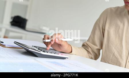Nahaufnahme eines jungen Mannes, der einen Stift hält und einen Taschenrechner benutzt, der vor ihm steht, ein Mann, der einen Stift hält und einen Taschenrechner benutzt. Stockfoto