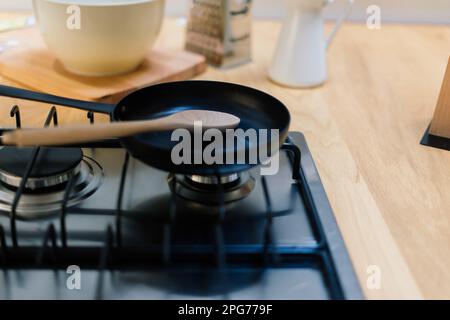 Spachtel in einer Pfannenpfanne mit Teflonbeschichtung auf Gasherd gegen Löffel, der in einer kleinen Küche hängt Stockfoto