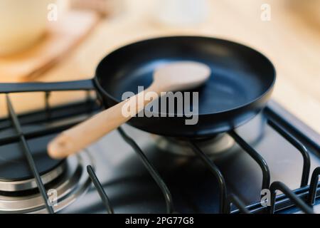 Spachtel in einer Pfannenpfanne mit Teflonbeschichtung auf Gasherd gegen Löffel, der in einer kleinen Küche hängt Stockfoto