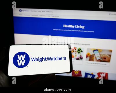 Person, die ein Mobiltelefon mit dem Logo von WW International Inc. Besitzt (Weight Watchers) auf dem Bildschirm vor der Business-Webseite. Konzentrieren Sie sich auf das Display des Telefons. Stockfoto