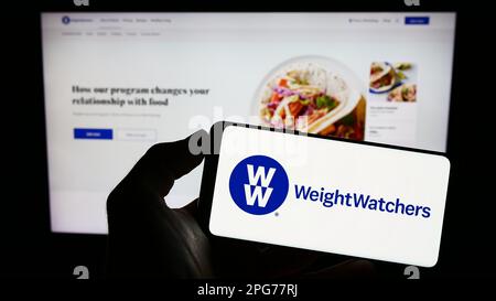 Person, die ein Mobiltelefon mit dem Logo von WW International Inc. Besitzt (Weight Watchers) auf dem Bildschirm vor der Business-Webseite. Konzentrieren Sie sich auf das Display des Telefons. Stockfoto