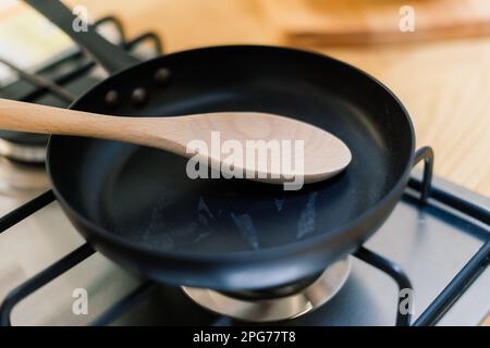 Spachtel in einer Pfannenpfanne mit Teflonbeschichtung auf Gasherd gegen Löffel, der in einer kleinen Küche hängt Stockfoto