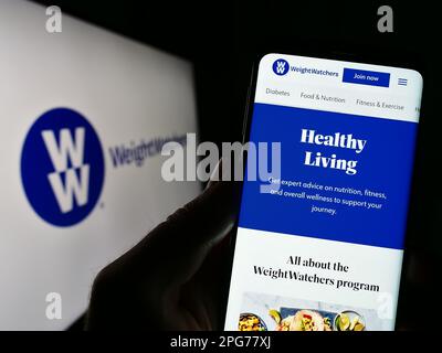 Person, die ein Mobiltelefon mit der Webseite von WW International Inc. Besitzt (Weight Watchers) auf dem Bildschirm vor dem Logo. Konzentrieren Sie sich auf die Mitte des Telefondisplays. Stockfoto