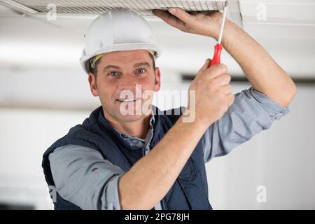 Glücklicher männlicher Arbeiter, der den Deckenluftfilter entfernt Stockfoto