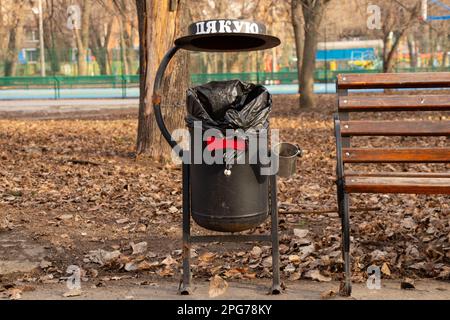 Mülleimer im Park in der Nähe einer Bank im Herbst in der Stadt Dnipro Ukraine, das Wort Danke auf Ukrainisch Stockfoto