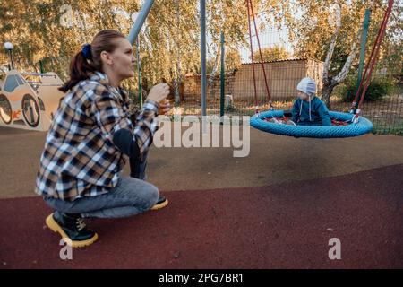 Süßer kleiner Junge mit Down-Syndrom mit seiner Mutter, schaukelt auf einer Schaukel, Seifenblasen Stockfoto